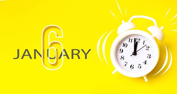 6 января. День 6 месяца, дата календаря. Белый будильник с календарным днем на желтом фоне. Минималистическое понятие времени, крайнего срока, времени на работу, утро. Концепция зимнего месяца, дня года - Фото, изображение