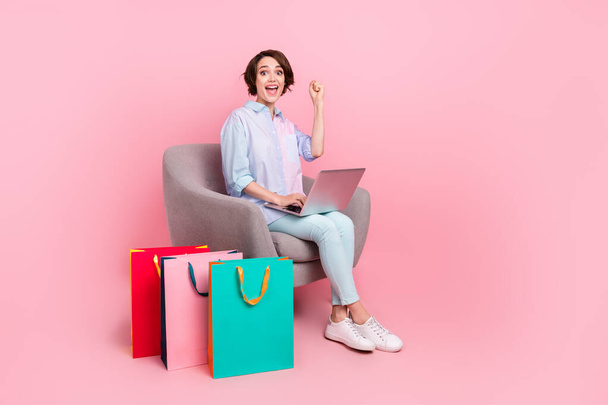 Full length body size photo woman sitting with packages working on computer gesturing like winner isolated pastel pink color background - Foto, Bild