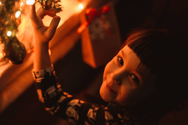 Boldog kislány az ablakban karácsonykor mosolyogva egy ajándékkal a kezében. Kívánj egy új évet.. - Fotó, kép