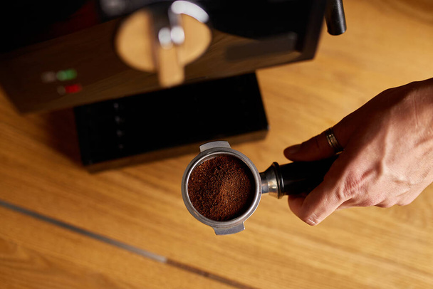 Ženské ruce drží portafilter a dělat čerstvé aromatické kávy doma pomocí moderního kávovaru, Muž barista ruční výroba espresso z mletého kávovaru v moderní kavárně - Fotografie, Obrázek