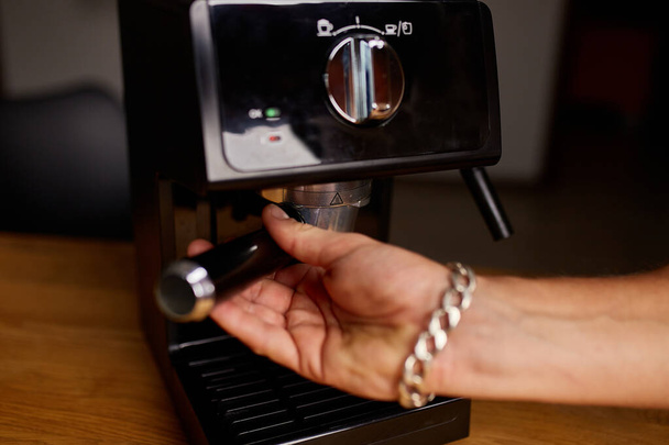 Mains féminines tenant portafilter et faisant du café aromatique frais à la maison à l'aide d'une cafetière moderne, Homme barista main faisant espresso à partir de la cafetière moulue à caf moderne - Photo, image