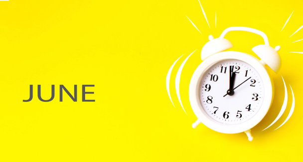 Kesäkuussa. Kuukausi, kalenterikuukausi. Valkoinen herätyskello kalenteripäivällä keltaisella taustalla. Minimalistinen käsitys ajasta, määräajasta, työajasta, aamusta. Kesä, kuukauden vuoden käsite - Valokuva, kuva