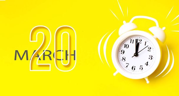 20 marca. Dzień 20 miesiąca, data kalendarza. Biały budzik z dniem kalendarzowym na żółtym tle. Minimalistyczna koncepcja czasu, terminu, czasu do pracy, poranka. Wiosenny miesiąc, koncepcja dnia roku - Zdjęcie, obraz