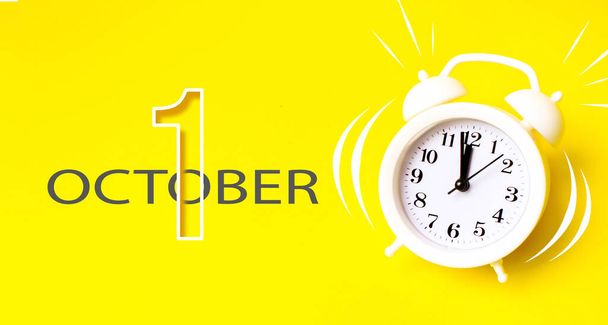 1 de octubre. Día 1 del mes, fecha del calendario. Reloj despertador blanco con día calendario sobre fondo amarillo. Concepto minimalista de tiempo, plazo, hora de trabajar, mañana. Mes de otoño, concepto del día del año - Foto, imagen