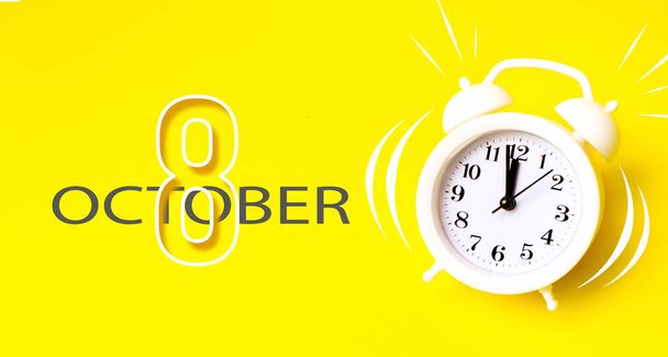 10月8日。月の8日、カレンダーの日付。黄色の背景にカレンダー日とホワイト目覚まし時計。時間、期限、仕事への時間、朝の最小限の概念。秋の月、その年のコンセプトの日 - 写真・画像