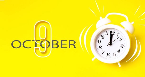 9. lokakuuta. Päivä 9 kuukauden, Kalenteri päivämäärä. Valkoinen herätyskello kalenteripäivällä keltaisella taustalla. Minimalistinen käsitys ajasta, määräajasta, työajasta, aamusta. Syksyn kuukausi, vuoden päivä käsite - Valokuva, kuva