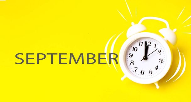 Syyskuussa. Kuukausi, kalenterikuukausi. Valkoinen herätyskello kalenteripäivällä keltaisella taustalla. Minimalistinen käsitys ajasta, määräajasta, työajasta, aamusta. Syksy, kuukauden vuoden käsite - Valokuva, kuva