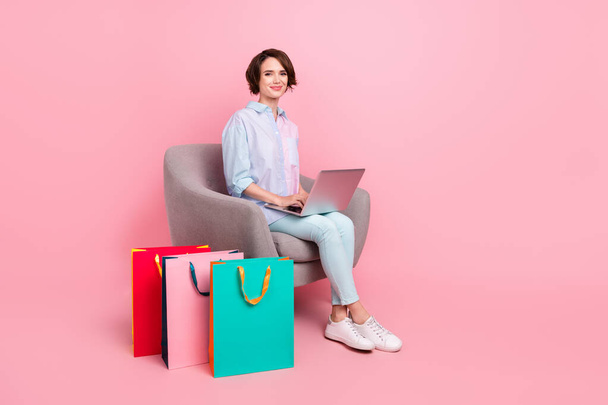 Full length body size photo woman sitting with packages typing on computer isolated pastel pink color background - Foto, Imagem