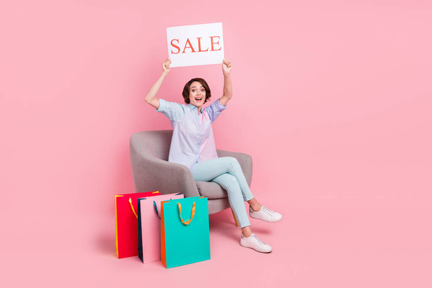 Full length body size photo woman sitting after online shopping amazed showing sale placard isolated pastel pink color background - Valokuva, kuva
