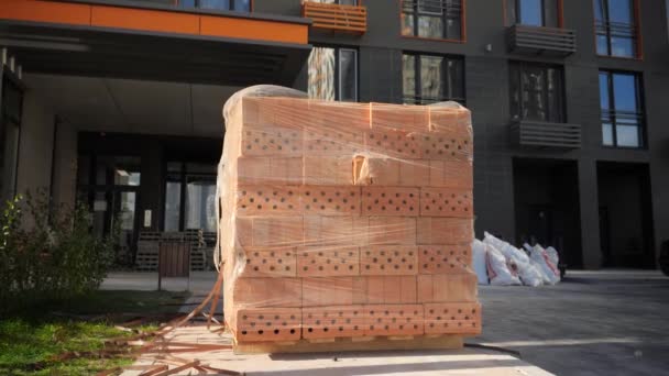 Pila grande o ladrillos de construcción rojos en paleta de madera en el sitio de construcción - Metraje, vídeo