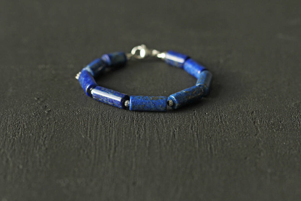 Blauwe natuurlijke lapis lazuli armband gemaakt van natuurlijke stenen ligt op een zwarte moderne betonnen achtergrond. Blauwe steen lapis lazuli. Handgemaakte sieraden van natuursteen. Handgemaakte armbanden. - Foto, afbeelding