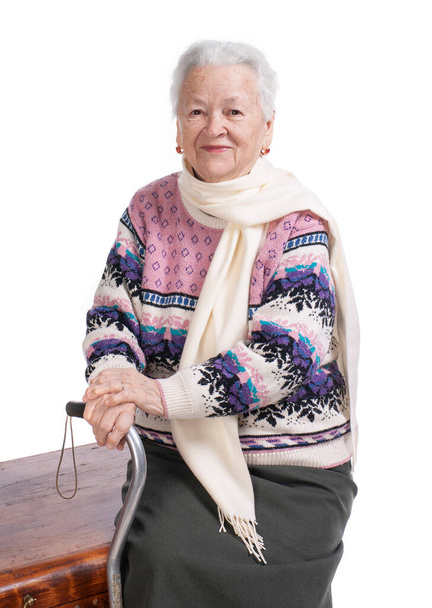 Vieja mujer sonriente con un bastón posando en el estudio sobre fondo blanco - Foto, Imagen