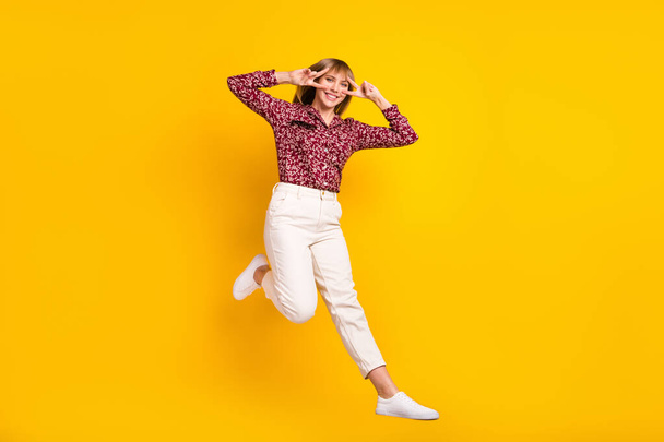 Full length body size photo jumping woman showing v-sign smiling isolated bright yellow color background - Foto, Imagem