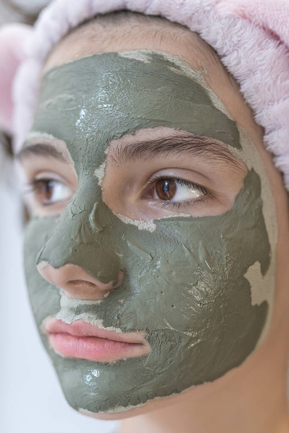 teenage girl of attractive appearance with brown eyes with mask of gray clay on her face in profile . female takes care of skin at home during isolation and pandemic. - Foto, Imagen