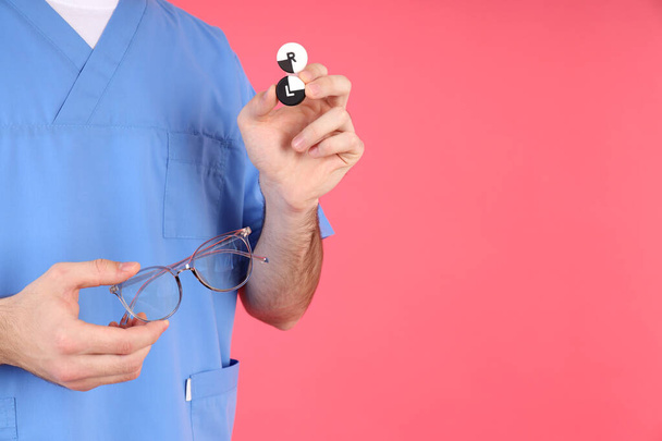 man verpleegster houdt bril en lenzen op roze achtergrond - Foto, afbeelding