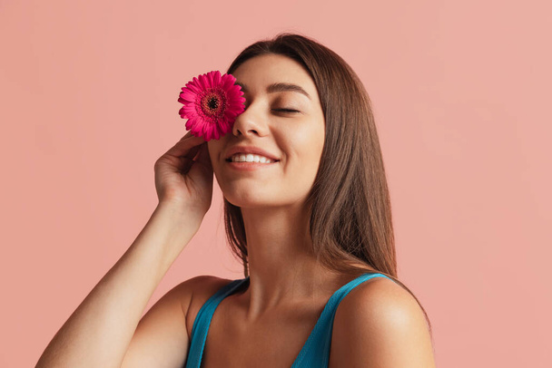 Half-length portrait of pretty girl with flower gerbera posing isolated over pink studio background. Natural beauty concept. - 写真・画像