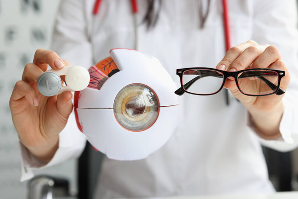 Oftalmólogo médico sosteniendo anteojos y lentes cerca de modelo artificial de primer plano - Foto, imagen