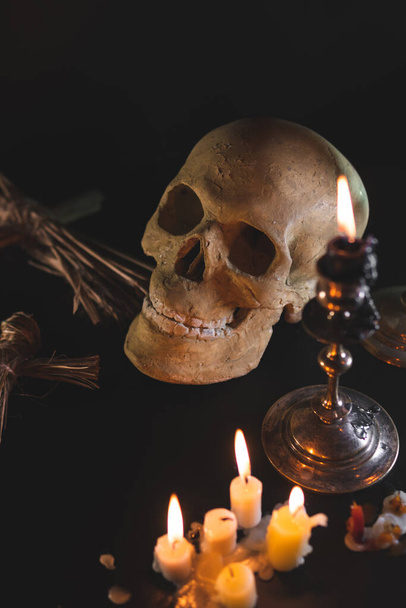 Old Skull and candle with incense on old altar plate which has dim light. Select focus, black background. Straw voodoo dolls. Copy space vertical photo - Photo, Image