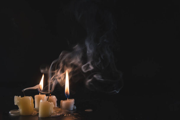 Ein paar Kerzen vor dunklem Hintergrund. Gebraucht, fast ausgelöscht. Ausgebrannt. Kopierraum. Mystische Rauchschwaden in der Dunkelheit. - Foto, Bild