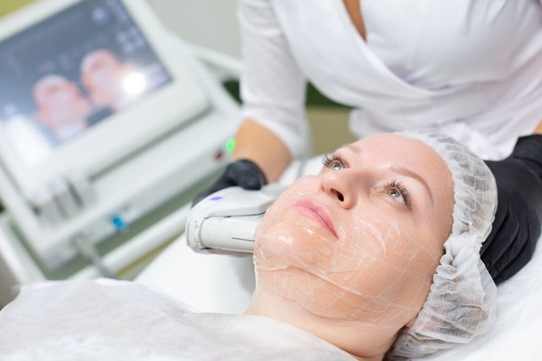 A woman in a cosmetology office receives a SMAS lifting procedure. Non-surgical ultrasound facelift, rejuvenation, moisturizing, getting rid of wrinkles, skin tone and elasticity - Zdjęcie, obraz