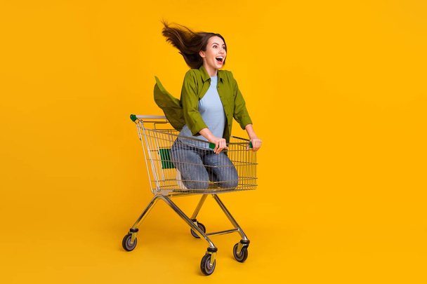 Full size photo of happy nice young woman look empty space ride trolley isolated on yellow color background - Foto, Imagem