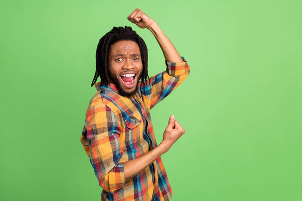 Photo of lucky funny dark skin man wear plaid shirt arm chin smiling rising fists isolated green color background - Foto, imagen
