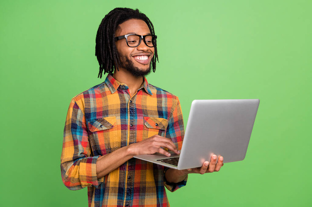 Photo of sweet cheerful dark skin man wear plaid shirt spectacles smiling typing modern device isolated green color background - Photo, image