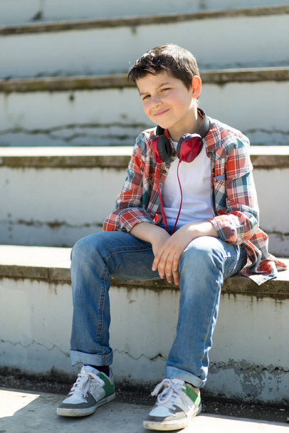 Cheerful boy sitting on bleachers at city park while looking at camera - Zdjęcie, obraz