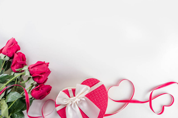 バレンタインデーの背景。白い背景にバラの花、ギフト、キャンドル、コンフェッティで作られたフラットレイフレーム。バレンタインデーグリーティングカードのコンセプト。トップビュー、コピースペース. - 写真・画像