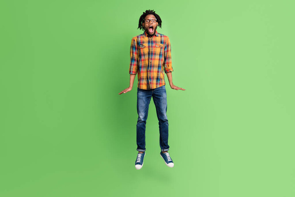 Photo of crazy astonished african guy jump scream open mouth wear plaid shirt jeans isolated green color background - Foto, imagen