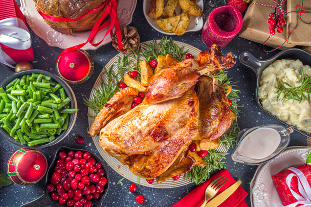 Christmas or New Year turkey dinner. Baked turkey with potato, red berries and sage leaves, on Christmas dinner table with Xmas tree, gift and candles background - Photo, Image