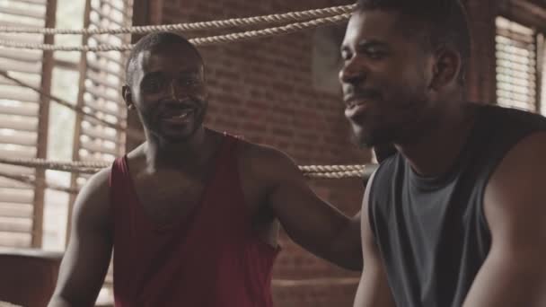 Plan de ralenti moyen de deux boxeurs afro-américains ayant une conversation amicale assis ensemble sur le ring après l'entraînement ou le sparring - Séquence, vidéo