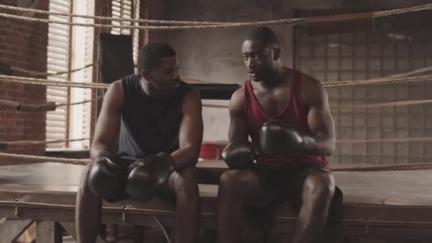 Lento tiro de dois boxers afro-americanos sentados no ringue de boxe em luvas discutindo e demonstrando socos durante o treinamento - Filmagem, Vídeo