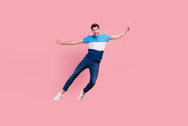 Full size photo of crazy brunet millennial guy jump wear polo jeans sneakers isolated on pink background - Foto, Imagen
