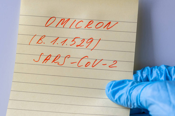 Tekst op stuk geel papier over nieuwe variant van de Covid-19 Omicron B.1.1.529. Nieuwe Zuid-Afrikaanse variant van het coronavirus, met een verhoogd risico op herbesmetting. Dokters hand in een blauwe handschoen - Foto, afbeelding