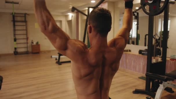 Nahaufnahme des Rückens eines jungen, muskulösen Mannes im Fitnessstudio, der auf einer Bank sitzend eine Langhantelpresse aus der Brust macht - Filmmaterial, Video