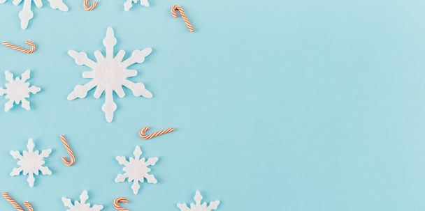Christmas composition. Banner made of snowflakes, red and white candies on blue background. Christmas, winter, new year concept. Minimal style. Flat lay, top view, copy space - Foto, imagen