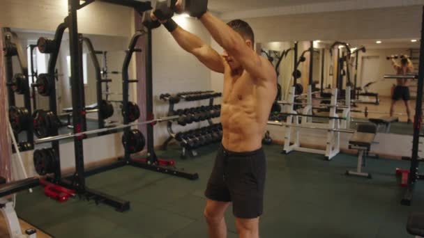 Giovane uomo muscolare che si allena in palestra e fa oscillazioni del braccio dritto con i manubri per allenare i muscoli deltoidi - Filmati, video