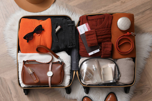 Open suitcase with folded clothes and accessories on floor, flat lay - Foto, imagen