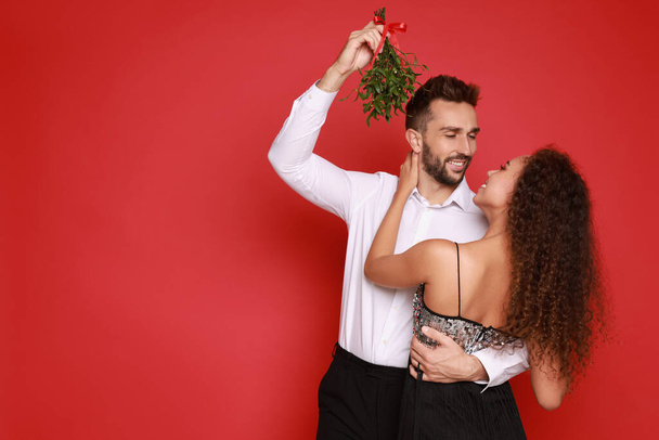 Lovely couple under mistletoe bunch on red background. Space for text - Fotografie, Obrázek