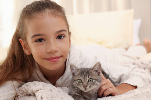 Cute little girl with kitten on white blanket at home. Childhood pet - Foto, Imagen
