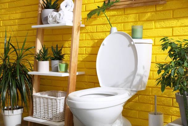 Stylish bathroom with toilet bowl and green plants near yellow brick wall. Interior design - Foto, immagini