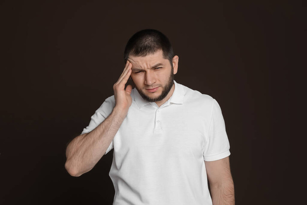Mann mit Kopfschmerzen auf dunkelbraunem Hintergrund - Foto, Bild