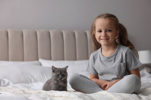 Cute little girl with kitten on bed at home. Childhood pet - Photo, image