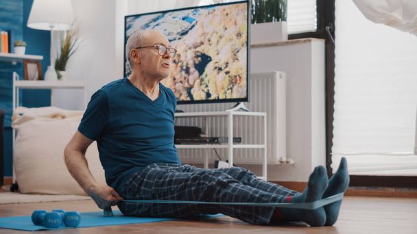 Uomo anziano che utilizza una fascia di resistenza per allungare braccia e gambe - Foto, immagini