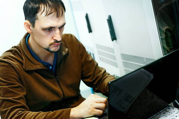 Egy munkahelyi programozó portréja. Hiteles jelenet. Egy informatikai szakember dolgozik egy laptopon a szerverszobában. - Fotó, kép