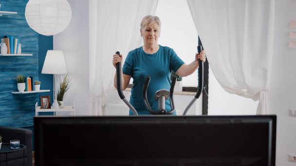 Aged woman using stationary bicycle to do workout training - Fotoğraf, Görsel