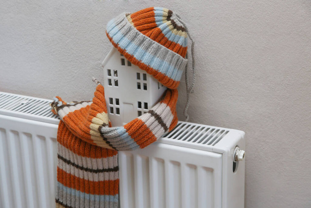 Figura de casa y ropa de abrigo en el radiador de calefacción. Gastos de calefacción y concepto de ahorro.  - Foto, Imagen