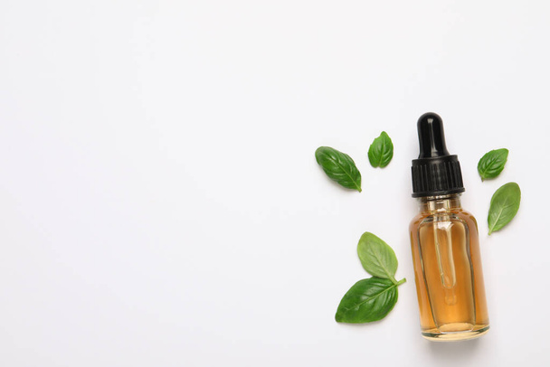 Bottle of essential basil oil and fresh leaves on white background, flat lay. Space for text - Foto, Imagem