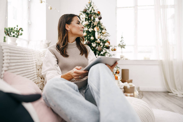 Beautiful woman relaxing on the sofa with digital tablet at Christmas - Fotó, kép